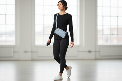Woman in black outfit with a blue bag walking in a bright room.